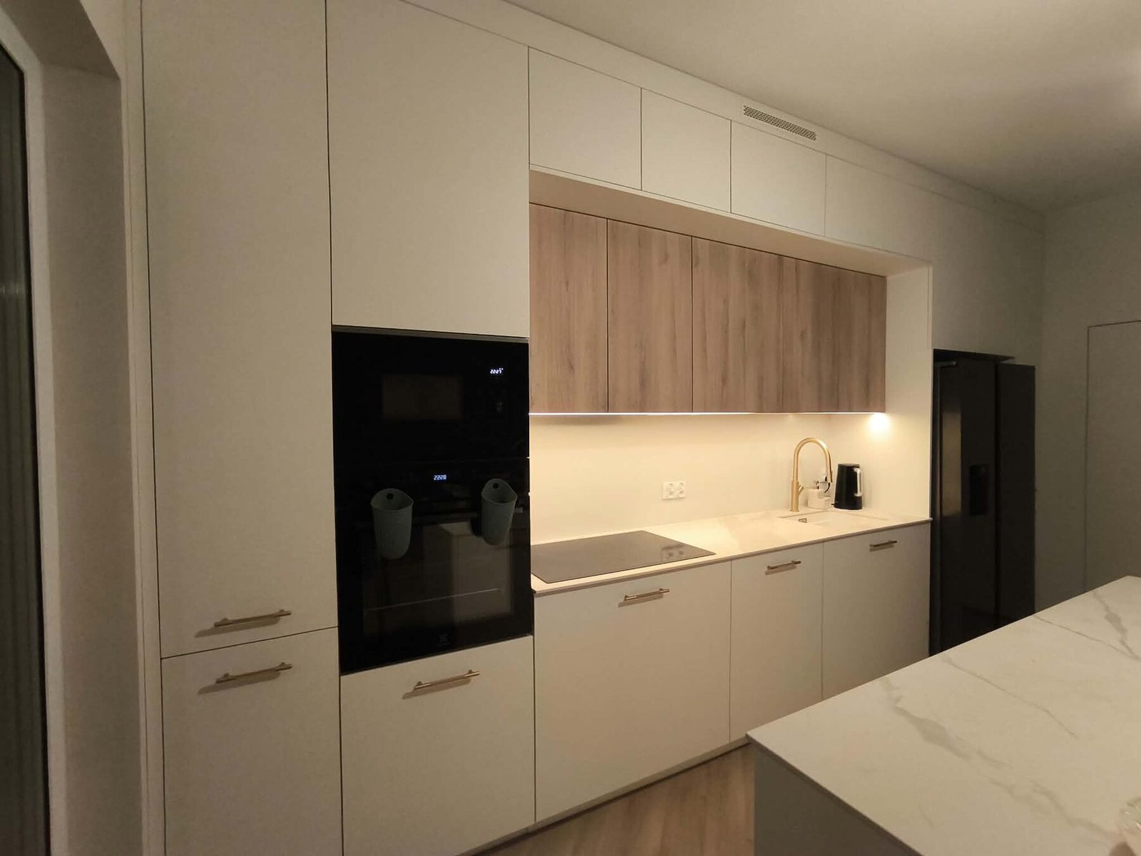 Kuchnia w bieli i drewnie — zabudowa z piekarnikiem i podświetlonymi szafkami